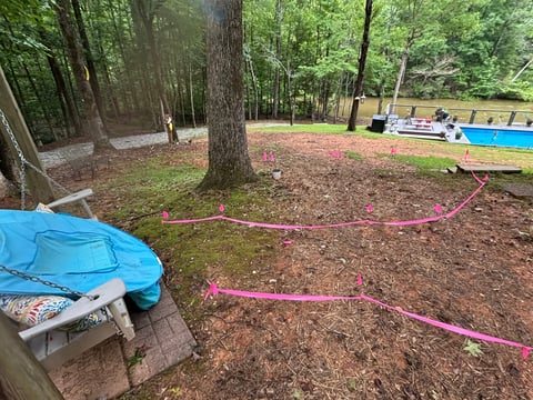 Outdoor adventure course in wooded area with blue tarps, pink rope obstacles, and large trees