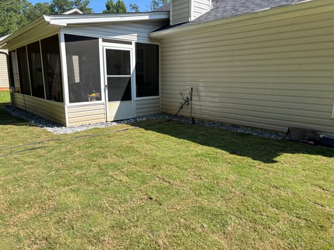 A residential home exterior with a screened porch addition, light-colored siding, and a mowed lawn in front