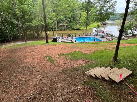Cornhole boards on forest ground with pool and waterfront view in residential backyard setting