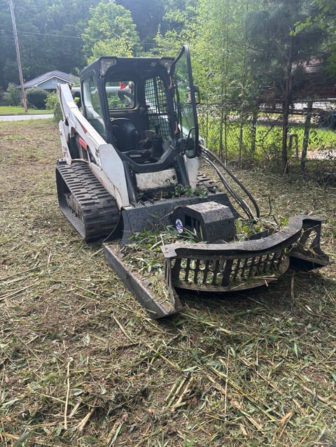 White and black compact tracked excavator with bucket attachment on grassy outdoor site near trees and fencing