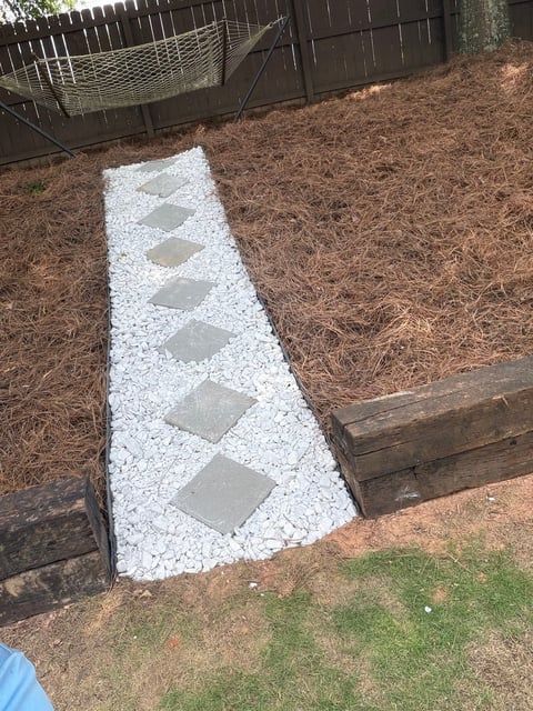 Pathway made of white gravel with gray stepping stones in a yard with mulch and metal fencing in background