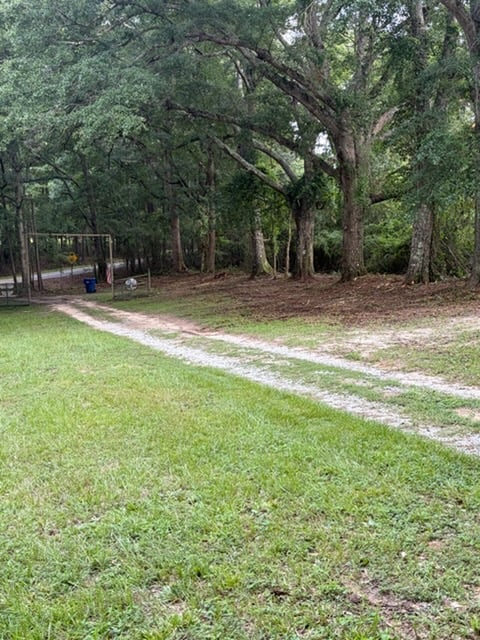 Grassy park pathway with dirt trail leading through mature oak trees and wooded area on a sunny day