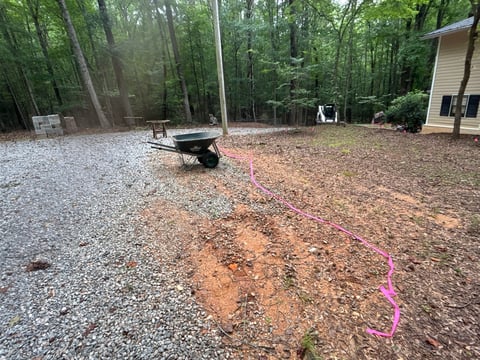 Wooded campsite with gravel area, fire pit, small building, and pink surveyors line marking ground